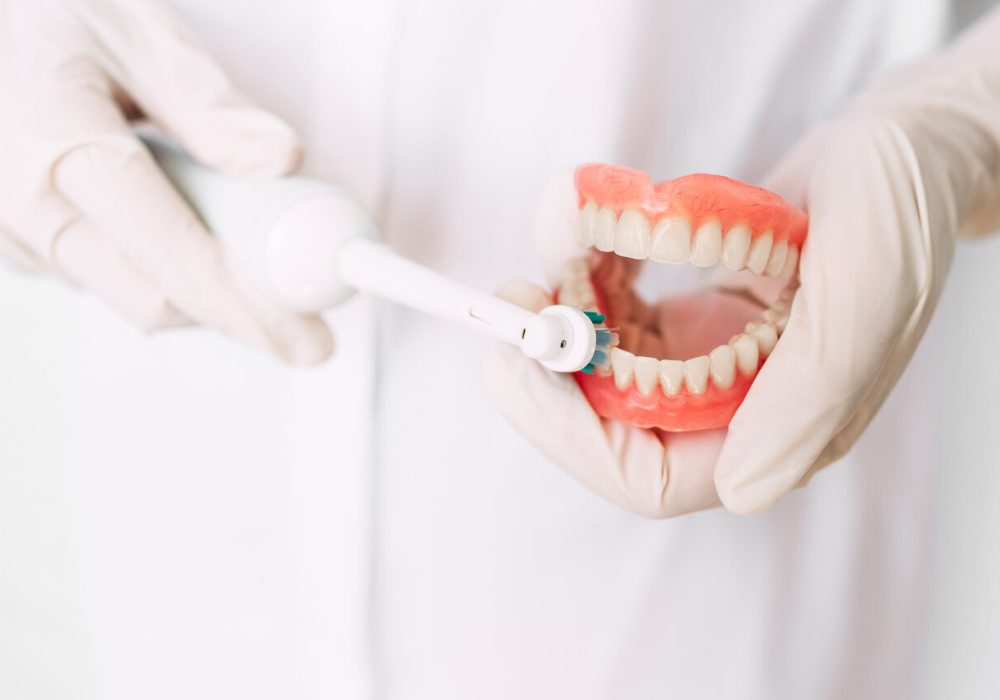 Oral hygiene. Dentist shows how to brush your teeth. Dental prosthesis in the hands of the doctor close-up. Dentistry conceptual photo. Prosthetic dentistry. False teeth